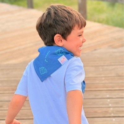 Menino de perfil com lenço azul com croissants e texto em francês