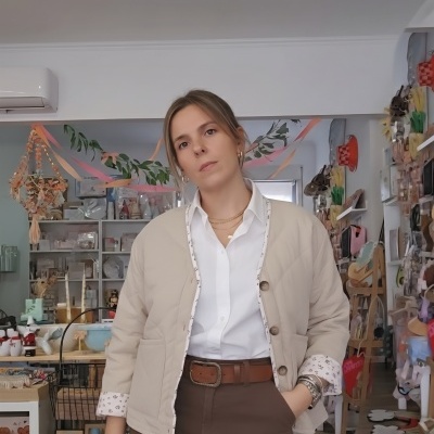 Mulher com casaco bege acolchoado, camisa branca e calças castanhas numa loja decorada