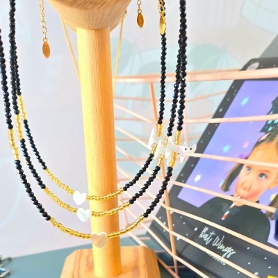 Colares em contas pretas e douradas com pendentes em forma de coração pendurados em suporte de madeira