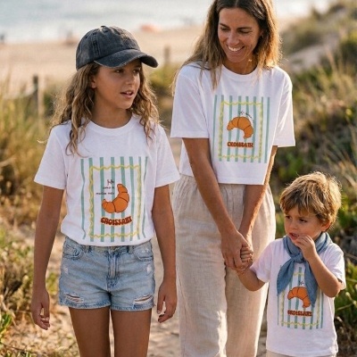 Família com t-shirts brancas com estampa de croissant numa praia.