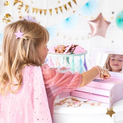 Criança a brincar com estojo de maquilhagem rosa e espelho numa mesa branca decorada