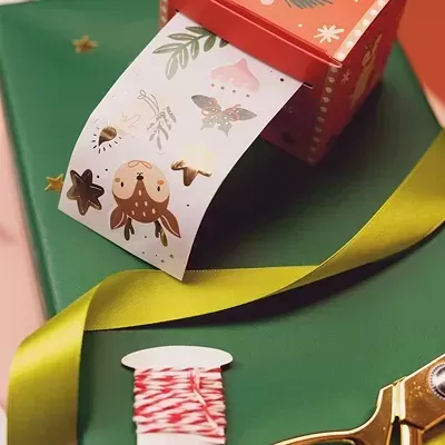 Caixa vermelha com fita adesiva natalícia e material de embrulho verde e amarelo