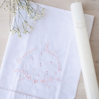 Toalha branca bordada com frase O meu Batismo e vela branca com etiqueta benedita em superfície de madeira