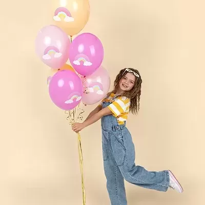Menina com macacão de ganga e balões cor-de-rosa e amarelos com arco-íris