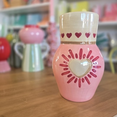 Vaso cerâmico rosa com decoração de corações vermelhos e coração em relevo no centro.