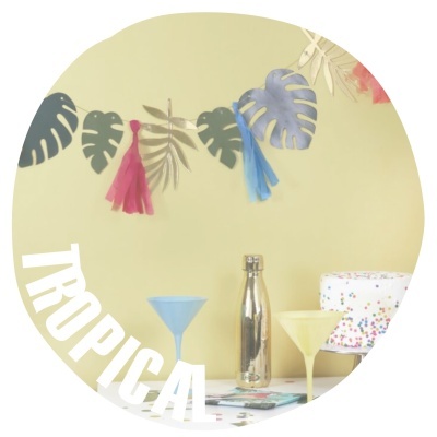 Decoração tropical com folhas, garrafa metálica e copos de cocktail coloridos