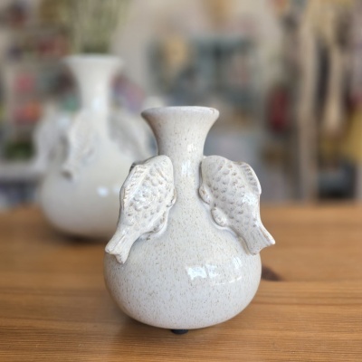 Vaso branco de cerâmica com pássaros em relevo e fundo desfocado.