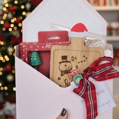 Conjunto de presente de Natal com tábua de madeira decorada, fita vermelha e caixa branca em envelope.