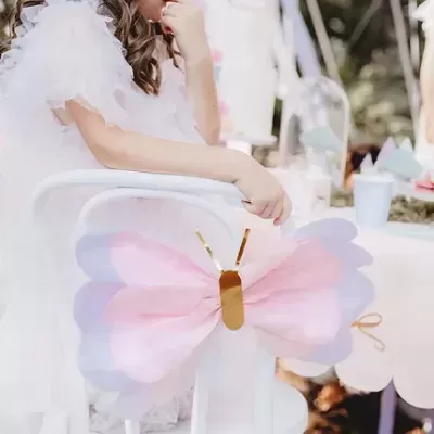Borboleta decorativa rosa e lilás presa em cadeira branca de festa ao ar livre