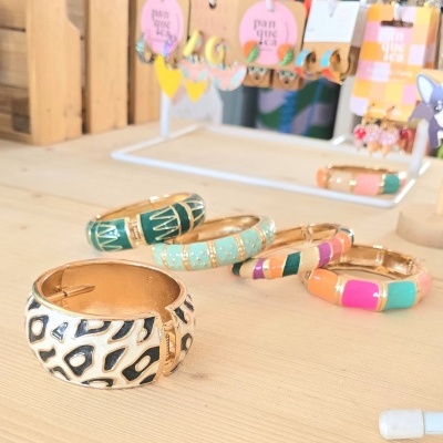 Braceletes coloridos em metal dourado com fundo de brincos em exposição