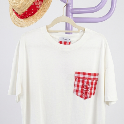 T-shirt branca com bolso xadrez vermelho e branco e chapéu de palha com lenço vermelho pendurados num porta-chapéus lilás