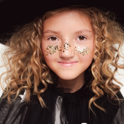 Criança com chapéu de bruxa preto e capa preta com purpurinas douradas no rosto