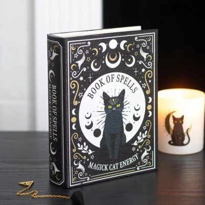 Livro decorativo com capa de gato preto e tema mágico ao lado de vela decorativa