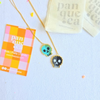 Colares com pendentes em forma de caveira colorida com correntes douradas sobre fundo branco.