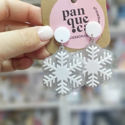 Brincos em forma de floco de neve com glitter prateado e base branca, em cartão rosa da marca panqueca acessórios.