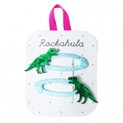 Dois ganchos de cabelo azuis com dinossauros verdes com lantejoulas em cartão branco