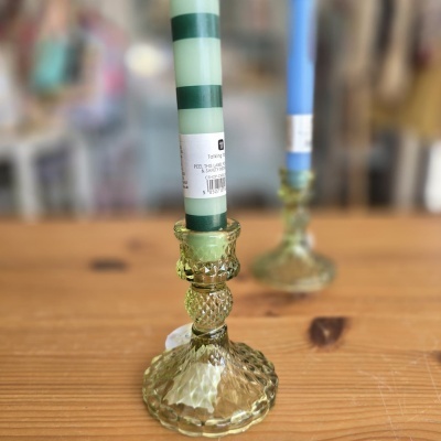 Dois castiçais de vidro verde com velas, uma verde às riscas e outra azul, sobre uma mesa de madeira.
