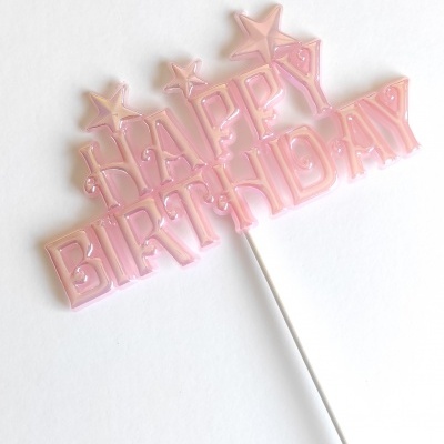 Topo de bolo cor-de-rosa translúcido com texto HAPPY BIRTHDAY em letras maiúsculas e estrelas