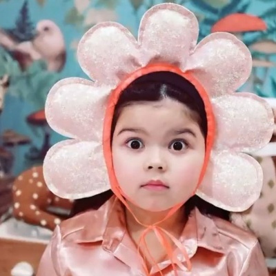 Crianças com chapéu de flor, coroa de unicórnio e decoração lúdica de parede colorida.