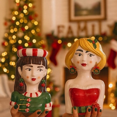 Duas figuras decorativas cerâmicas femininas com temas natalícios, em ambiente decorado de Natal.