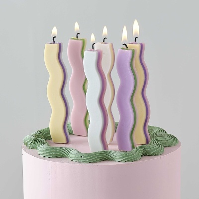 Bolo rosa claro com velas onduladas acesas em tons pastel