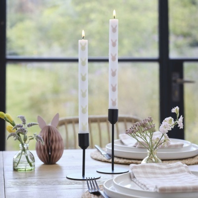 Mesa com castiçais pretos, velas brancas com coelhos e decoração de Páscoa