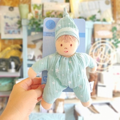 Boneco de tecido verde água com estampado de estrelas e rosto bordado, em embalagem azul e branca