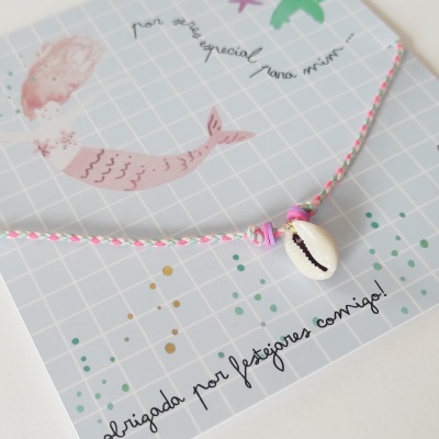 Pulsera de concha blanca con hilo rosa y blanco sobre tarjeta azul con sirena y texto en portugués