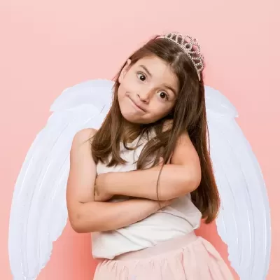 Menina com asas de anjo, tiara prateada, camisa branca e saia rosa claro sobre fundo rosa