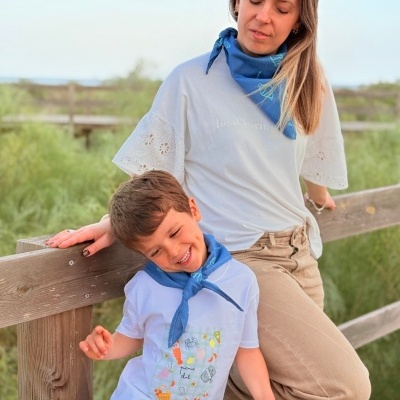 Criança e mulher com t-shirts brancas e bandanas azuis encostados numa vedação de madeira ao ar livre