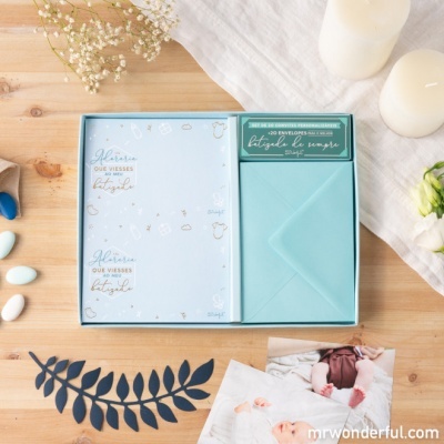 Conjunto de papelaria azul com envelopes e folhas decoradas em caixa azul sobre mesa de madeira com velas e decorações