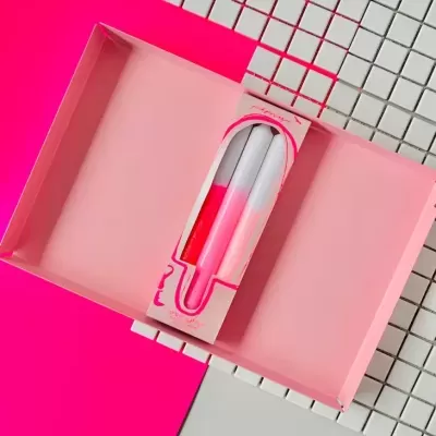 Caixa rosa aberta com pulseira de silicone branca e rosa dentro, sobre fundo quadriculado branco e superfície rosa