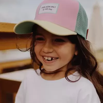 Menina sorridente a usar boné colorido com etiqueta 'COOL KIDS ONLY'