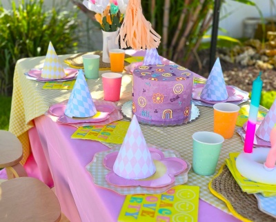 Mesa de festa colorida com bolo decorado e chapéus de festa com padrão de losangos