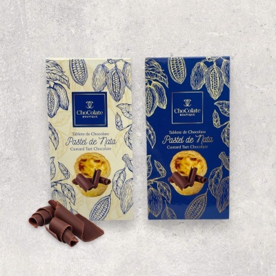 Duas embalagens de chocolate Pastel de Nata, uma creme e outra azul escuro, com pedaços de chocolate à frente.