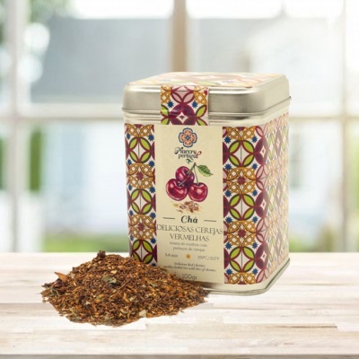 Caixa metálica de chá com padrão colorido e chá solto sobre mesa clara