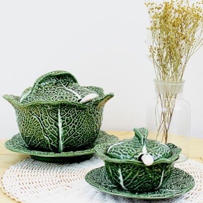 Conjunto de loiça verde com padrão de folhas sobre centro de mesa branco e jarro com flores secas