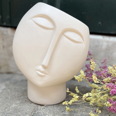 Vaso de cerâmica em forma de rosto estilizado creme junto a flores secas