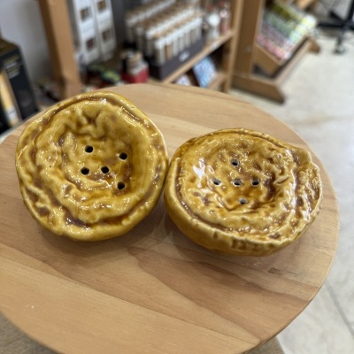 Duas tigelas cerâmicas amarelas com furos em cima de mesa de madeira.