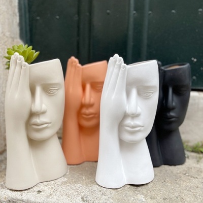 Vasos decorativos em forma de rostos humanos em várias cores com suculenta, em superfície de pedra