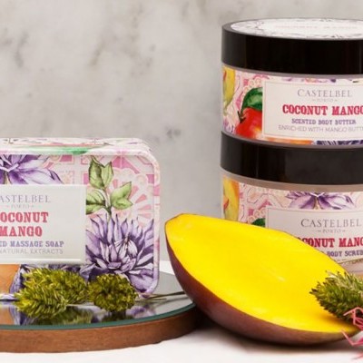 Produtos de cuidado corporal CASTELBEL Coconut Mango com sabonete e cremes em embalagem floral, manga cortada e elementos naturais sobre fundo mármore.