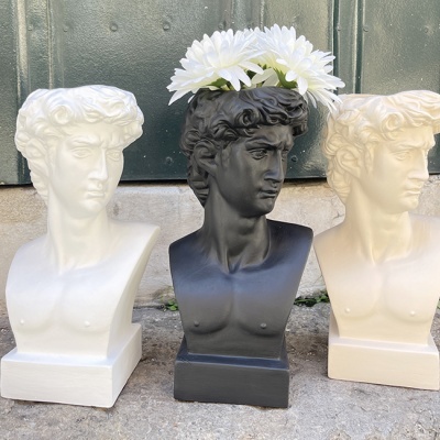 Três bustos decorativos estilo David de Michelangelo, dois brancos e um preto com flores brancas.