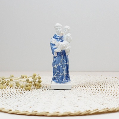 Estátua de santo azul com criança em tapete redondo e ramo seco