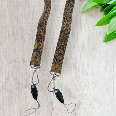 Dois cordões castanhos com padrões tradicionais e ganchos metálicos sobre madeira clara