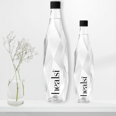 Duas garrafas de água de vidro com tampa preta e padrão facetado, ao lado de vaso com flores brancas