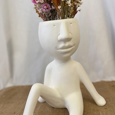 Vaso cerâmico branco em forma de figura humana sentada com flores secas coloridas na cabeça