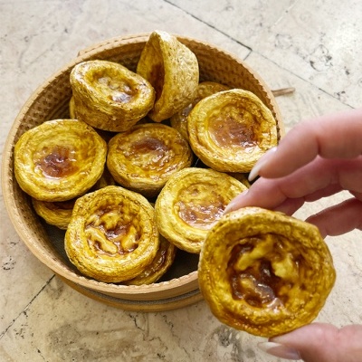Cesto de madeira com pastéis de nata dourados, mão a segurar um pasteis.