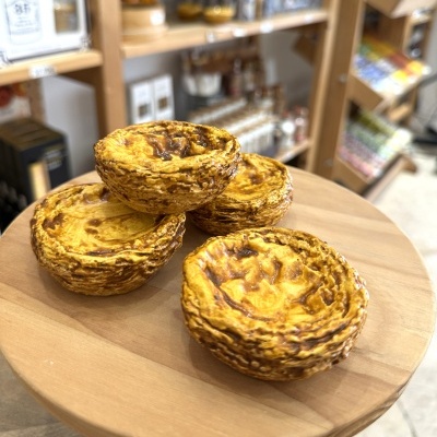 pastéis de nata sobre placa de madeira com prateleiras ao fundo