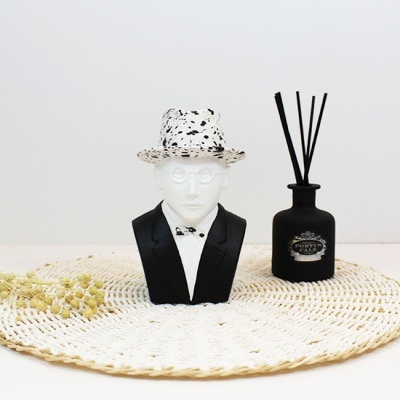 Busto decorativo com chapéu manchado preto e branco e difusor de aromas preto sobre tapete de croché