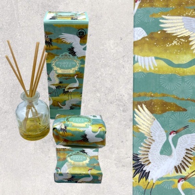 Difusor aromático de vidro com varetas e caixas decorativas verdes com ilustração de garças e detalhes dourados.